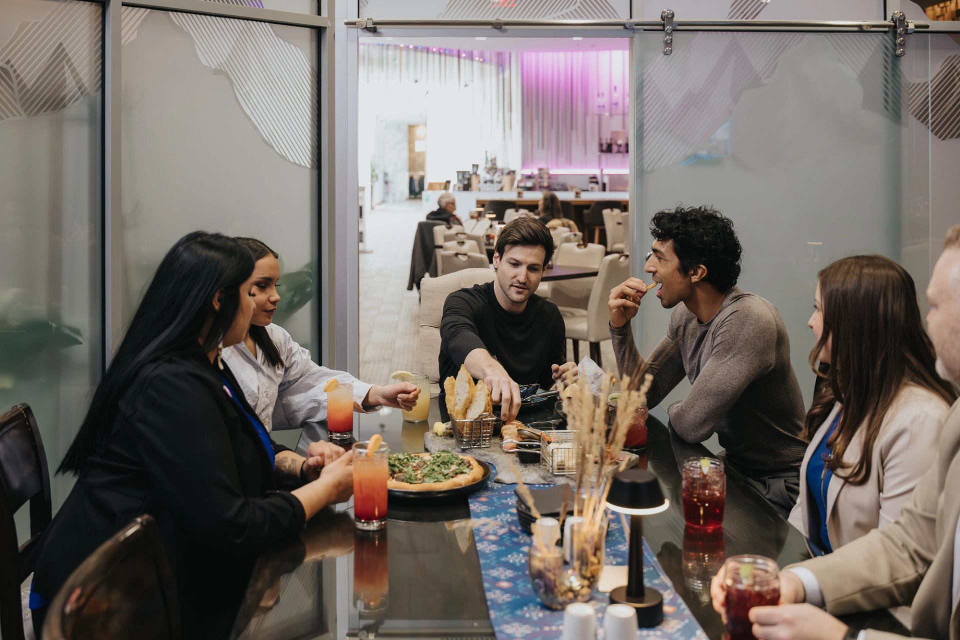 Group of people share pizza and drinks at a restaurant table with modern decor.