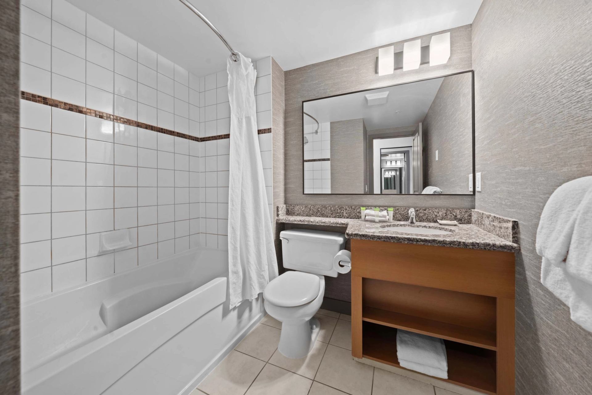 Bathroom with tiled bathtub, toilet, granite vanity, large mirror and towel rack.