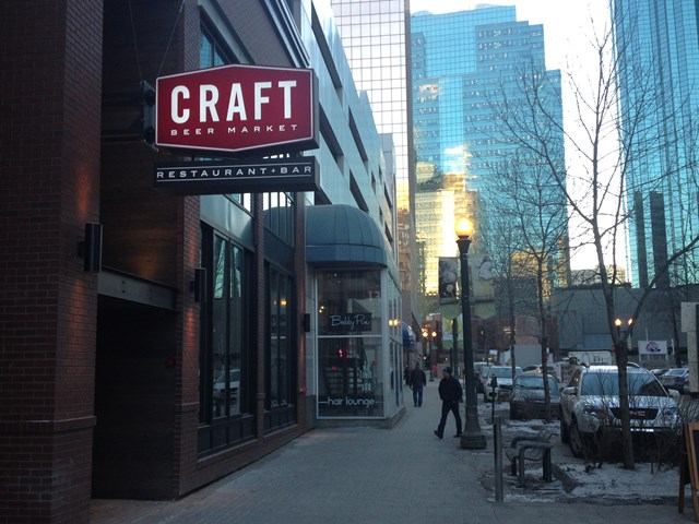 Craft Beer Market sign on city building with pedestrians and cars nearby.