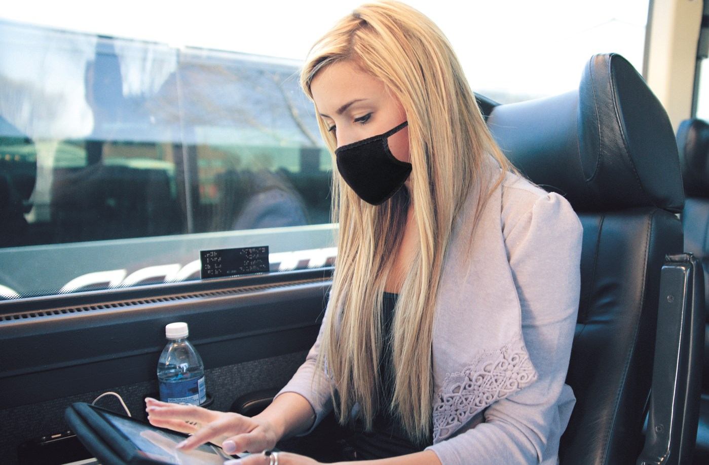 Passenger using tablet with water bottle on armrest aboard Red Arrow Motorcoach.