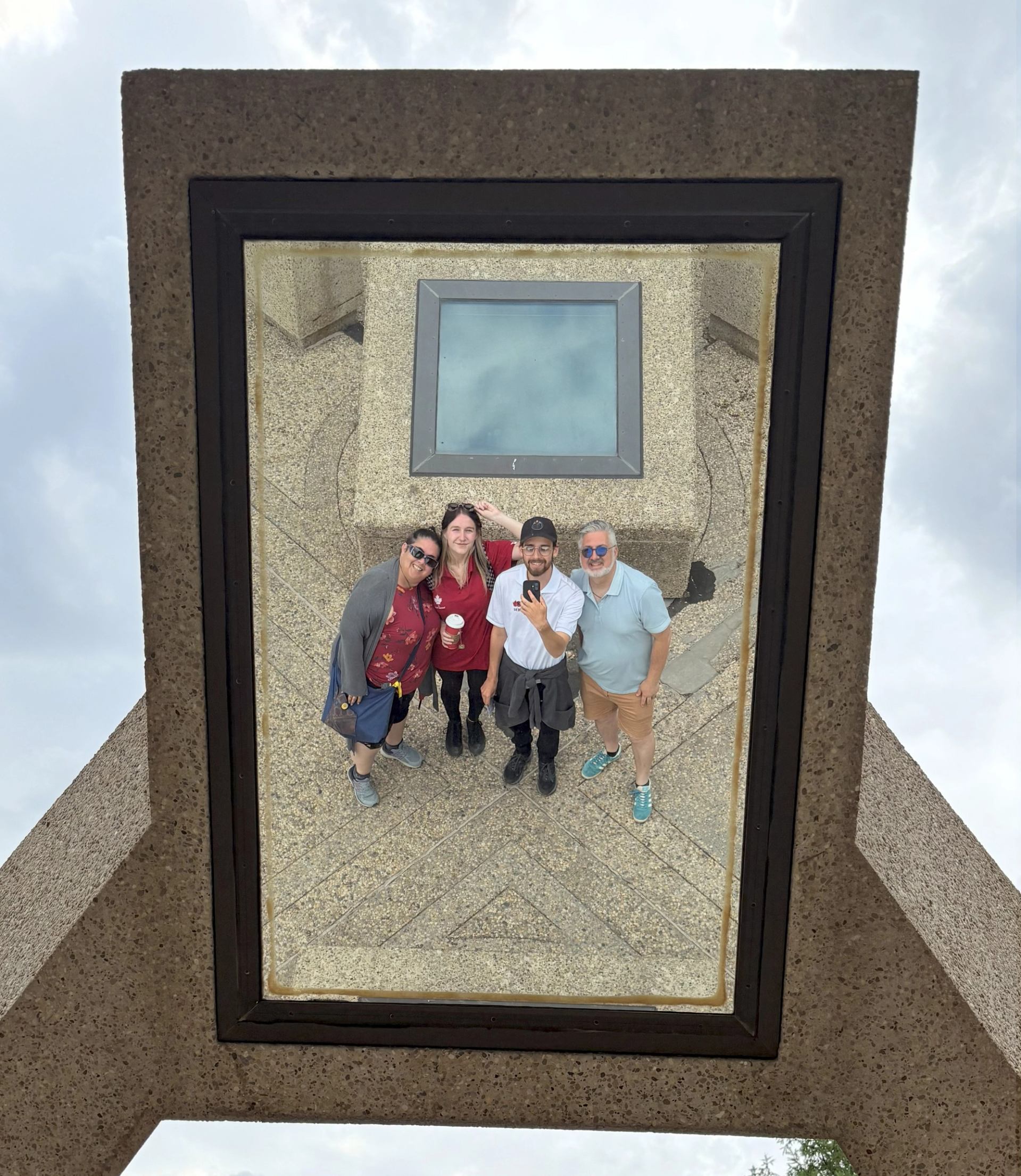 Four people reflected in a mirror beneath geometric architecture in Edmonton.