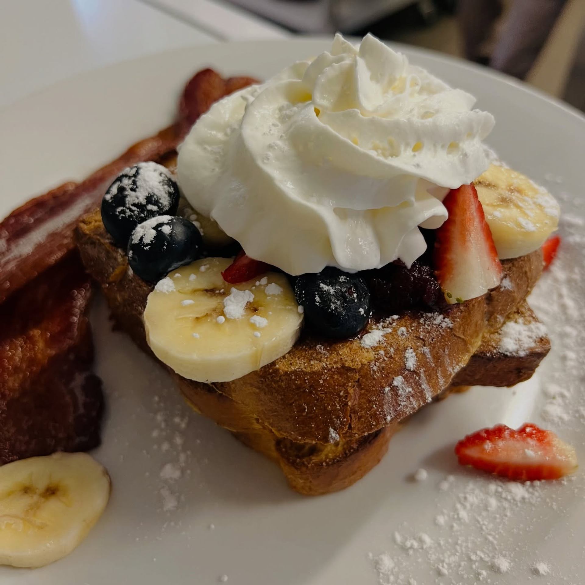 French toast topped with whipped cream, berries, banana slices, and bacon