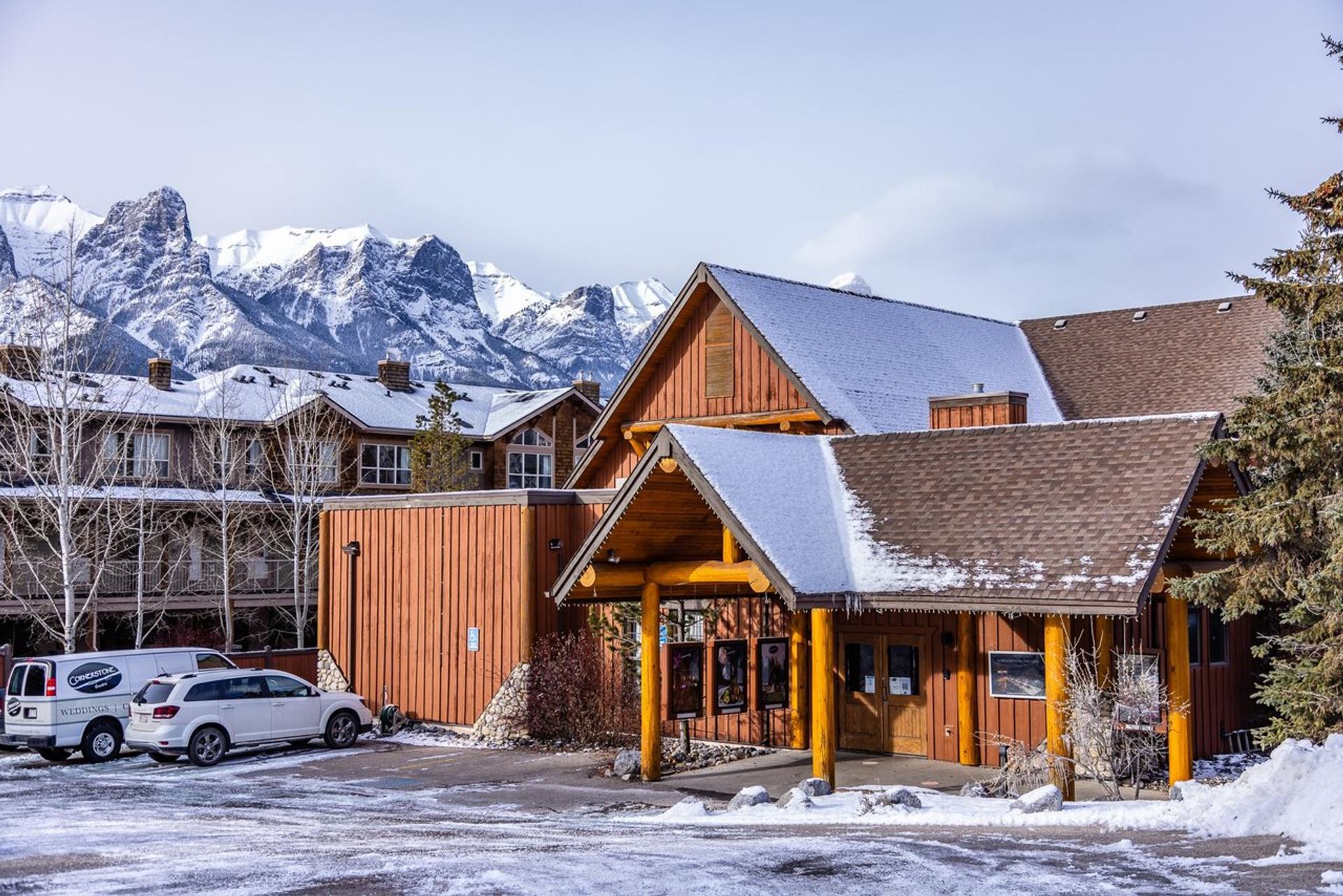 Wooden theatre building with snowy roof set against tall mountain scenery.