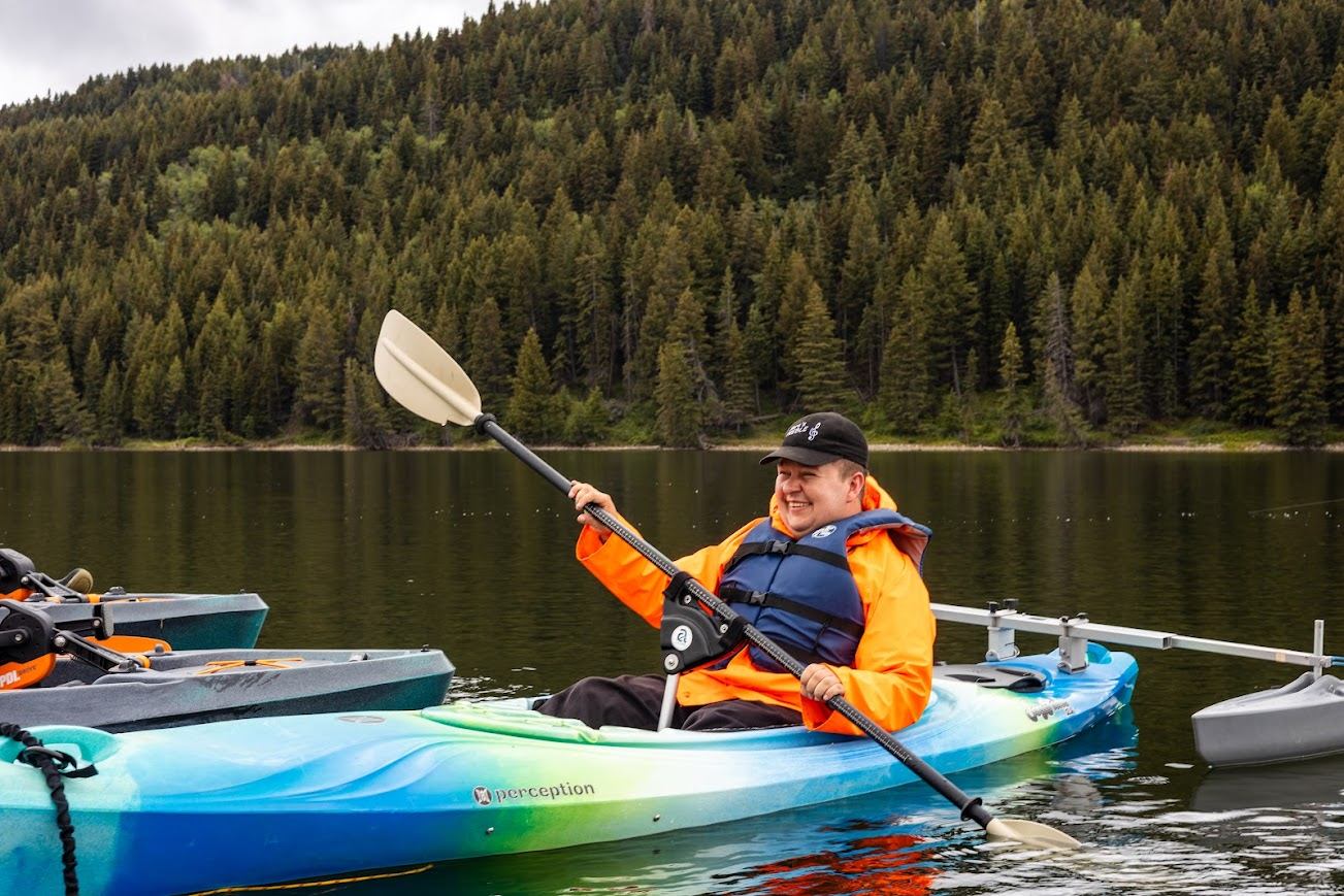 Person kayaking on a calm lake surrounded by dense evergreen forest.