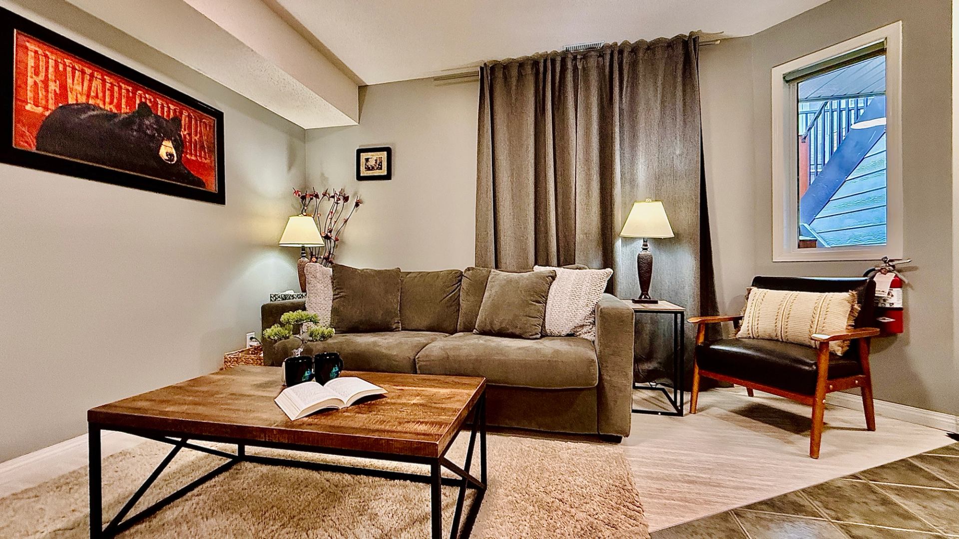 Living room with sofa, armchair, lamps and wooden coffee table holding an open book.