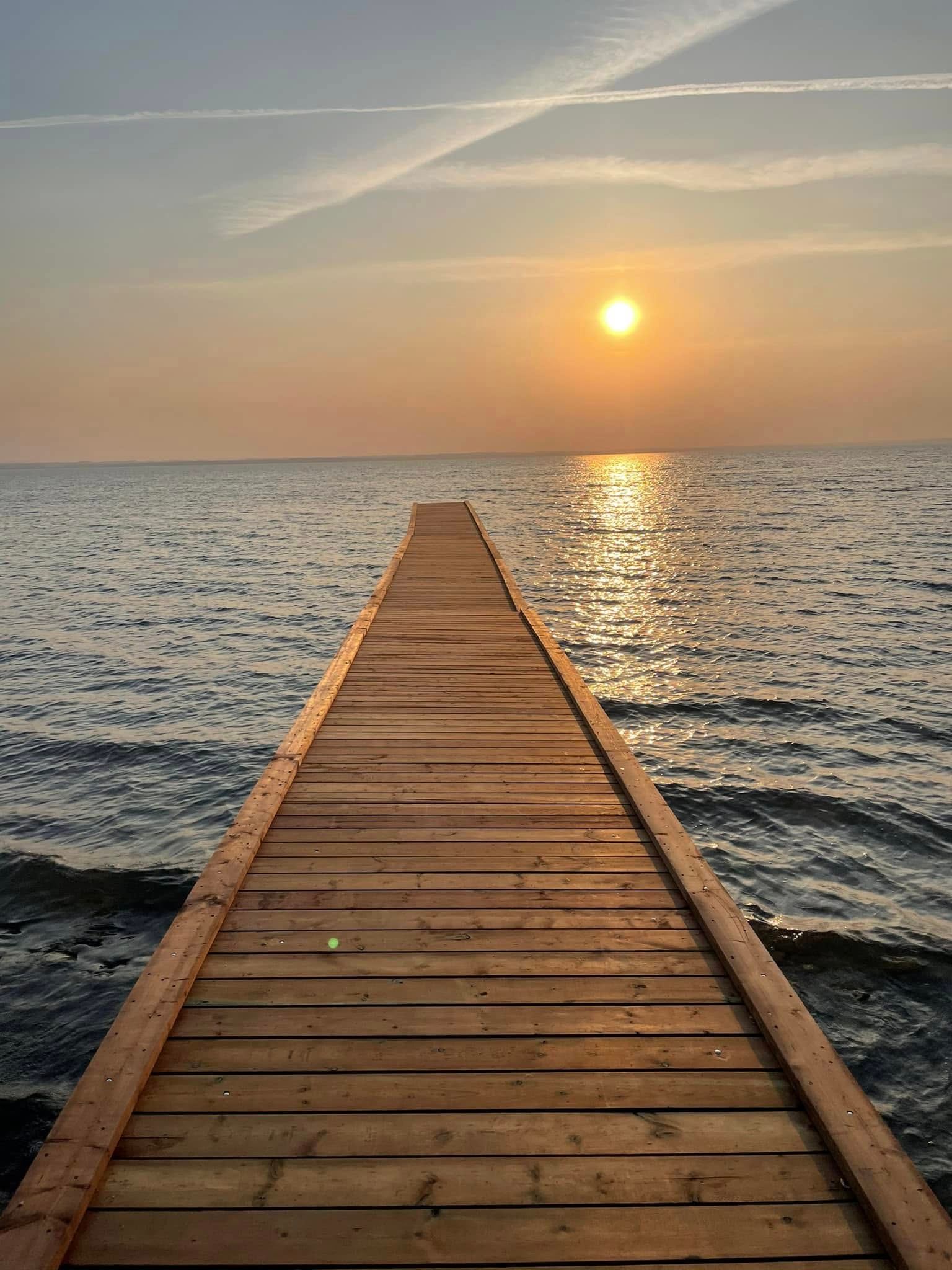 A wooden dock extends into calm water with the sun setting on the horizon at Wilson’s Beach Campground.