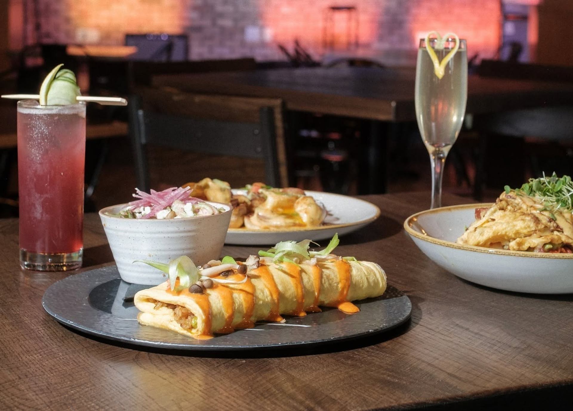 Plated omelette with sauce, side dishes and cocktails on a wooden restaurant table.