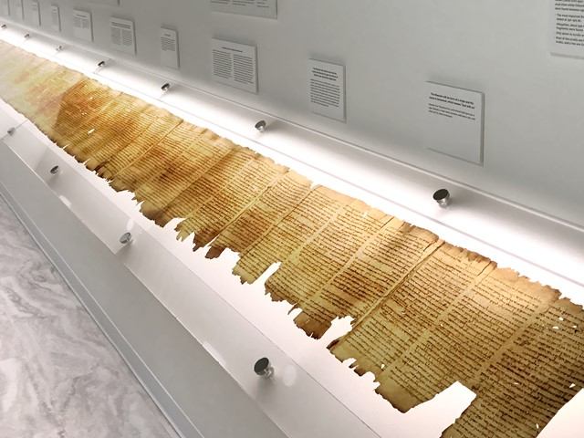 Long parchment manuscript in glass display case with wall labels above.