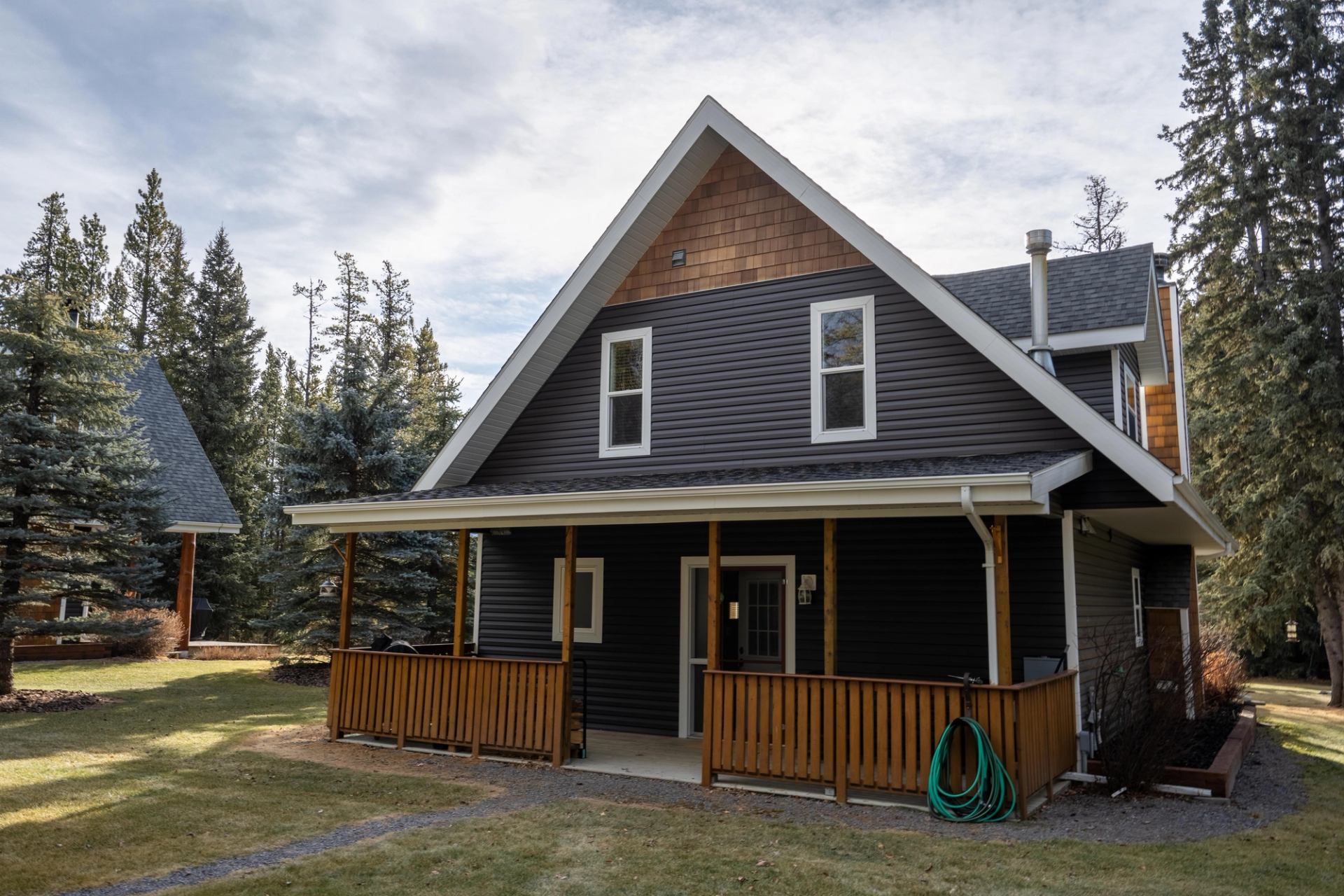 Wood-sided lodge with gabled roof, windows, and front porch in a wooded area.