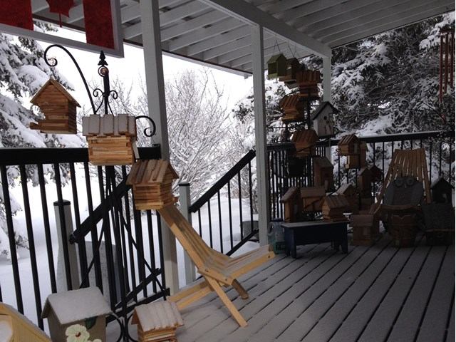 Snowy porch with wooden birdhouses, chairs, and a Canadian flag overhead.