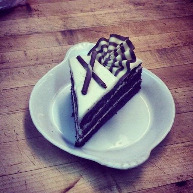 Layered chocolate cake with white frosting and chocolate drizzle on a white plate.