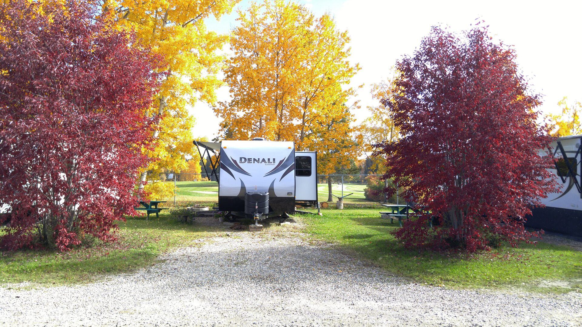An RV parked in an autumn campground surrounded by vibrant red and yellow trees.