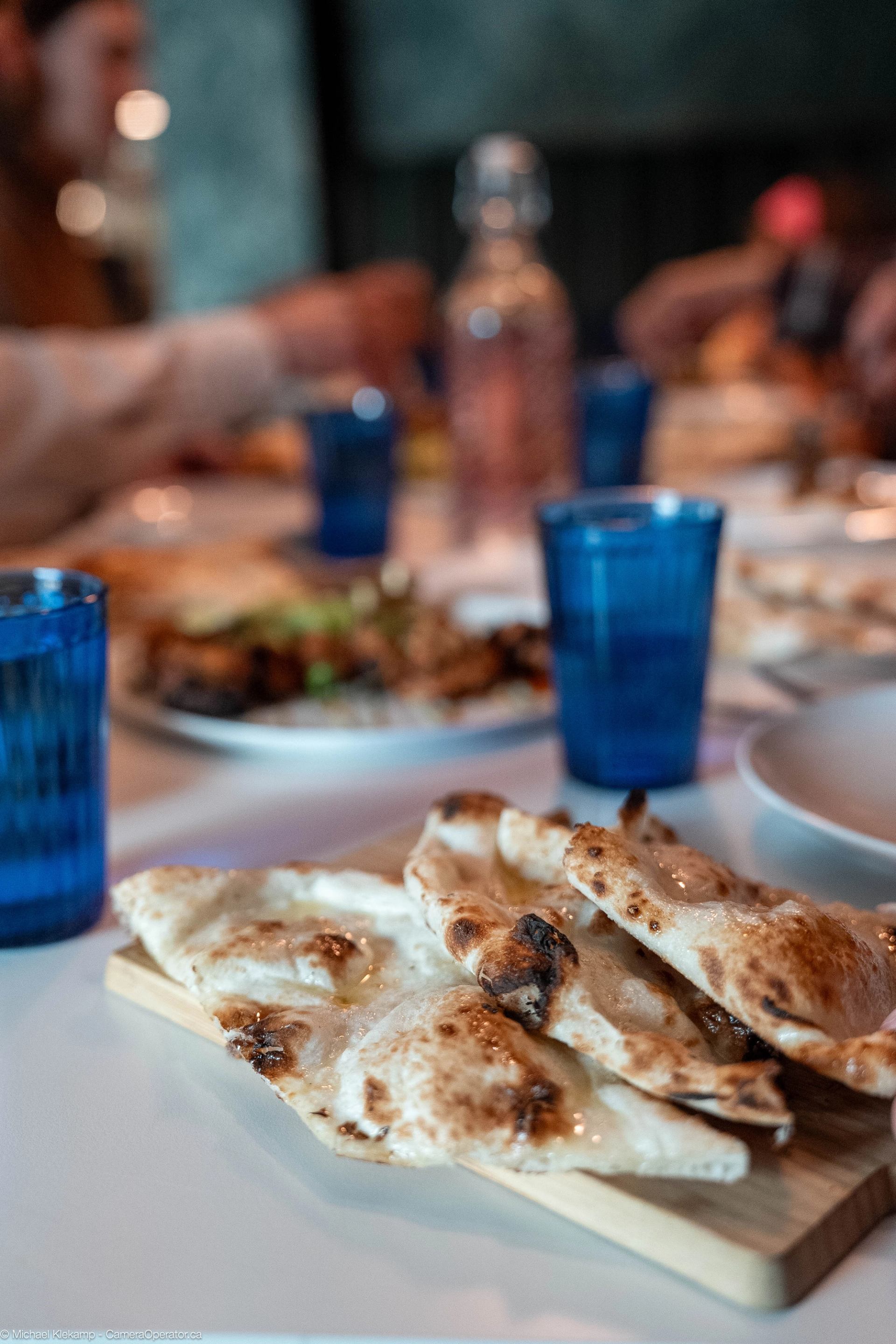 Close-up of freshly baked flatbreads on a wooden board with blue glasses and dishes in the background.