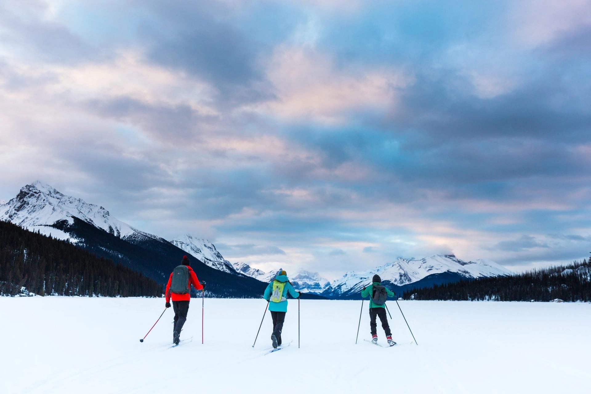 Three cross country skiers stop to take in the mountain view while skiing on Maligne Lake in Jasper National Park.