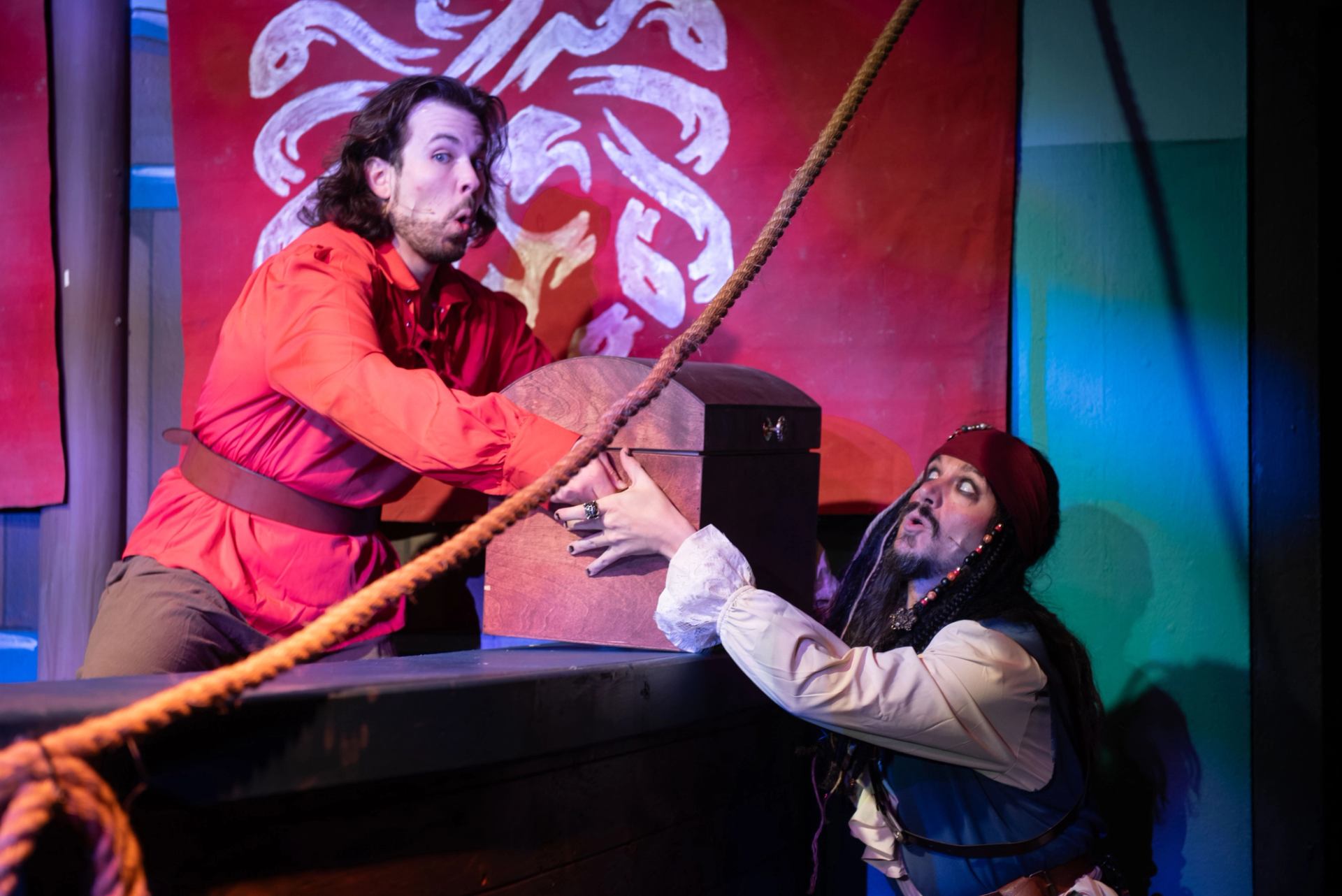 Two pirates pulling a chest on a colorful stage with ropes and banners