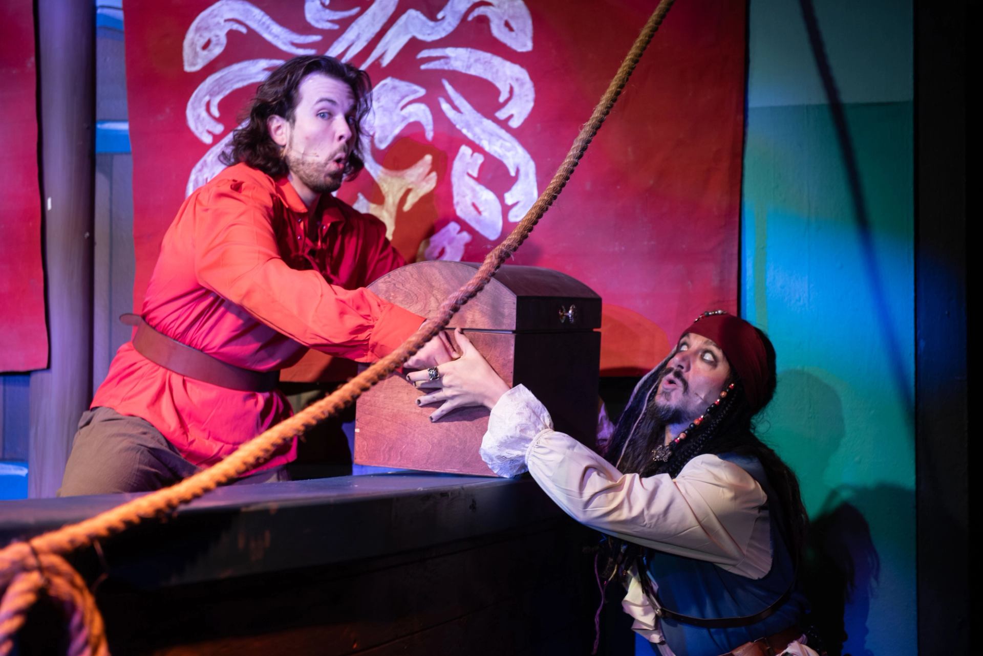 Two pirates pulling a chest on a colorful stage with ropes and banners