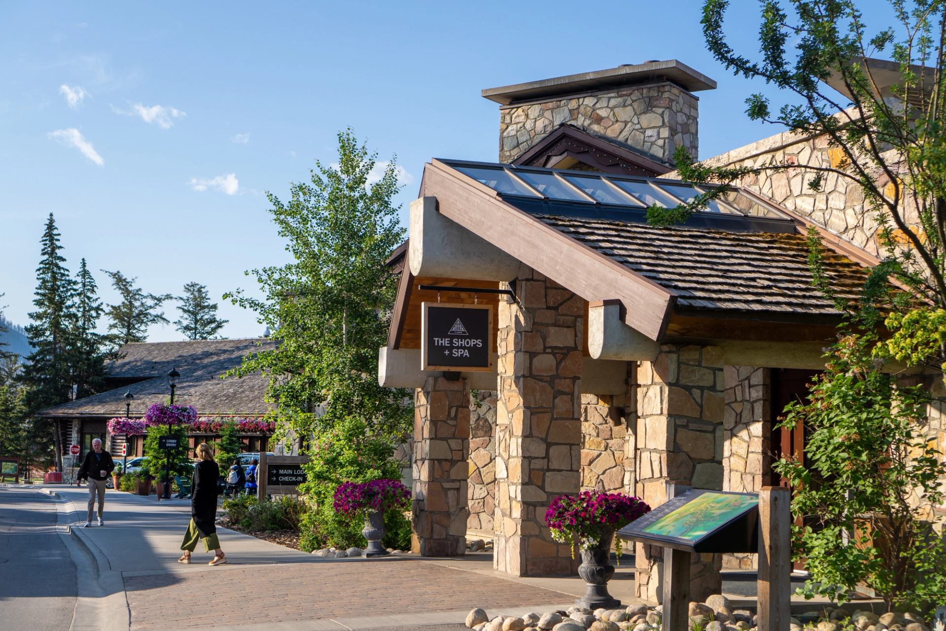 Fairmont Jasper Spa shops with stone buildings, flowers, and people walking on a sunny day.