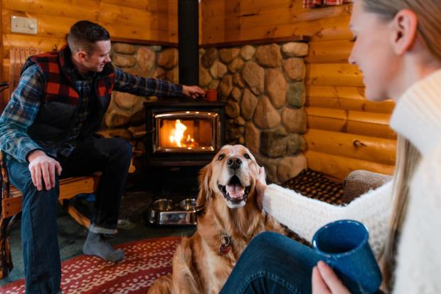 Couple and dog sitting by the fire inside a log cabin at the Baker Creek Mountain Resort