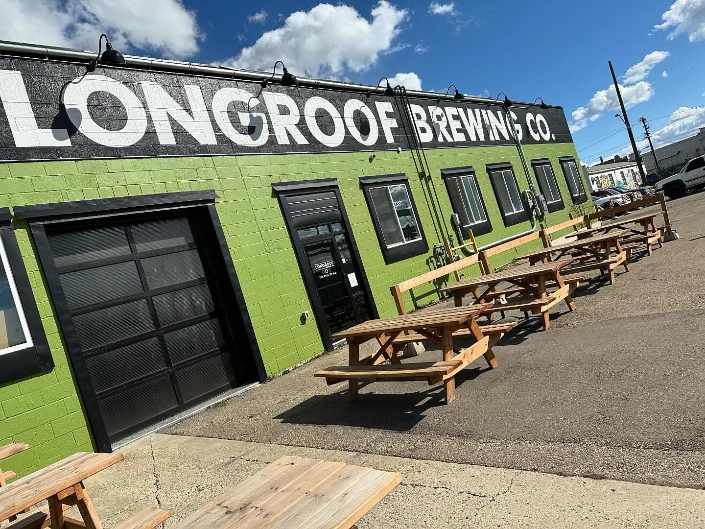 Exterior of Longroof Brewing Company with green facade and picnic tables outside.