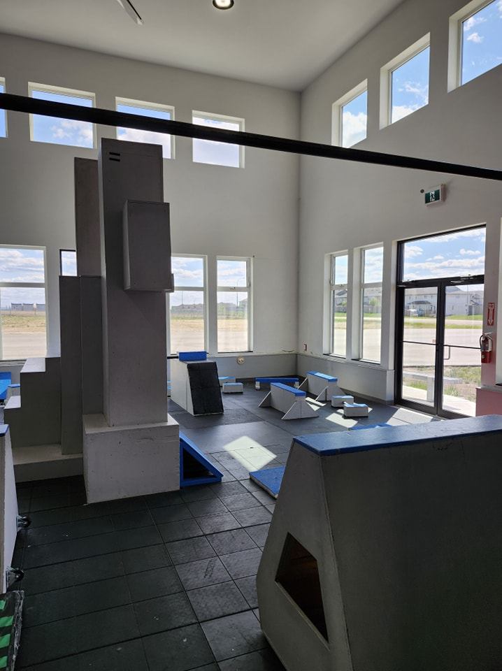 Indoor ninja warrior obstacle course with padded blocks and foam ramps near windows.