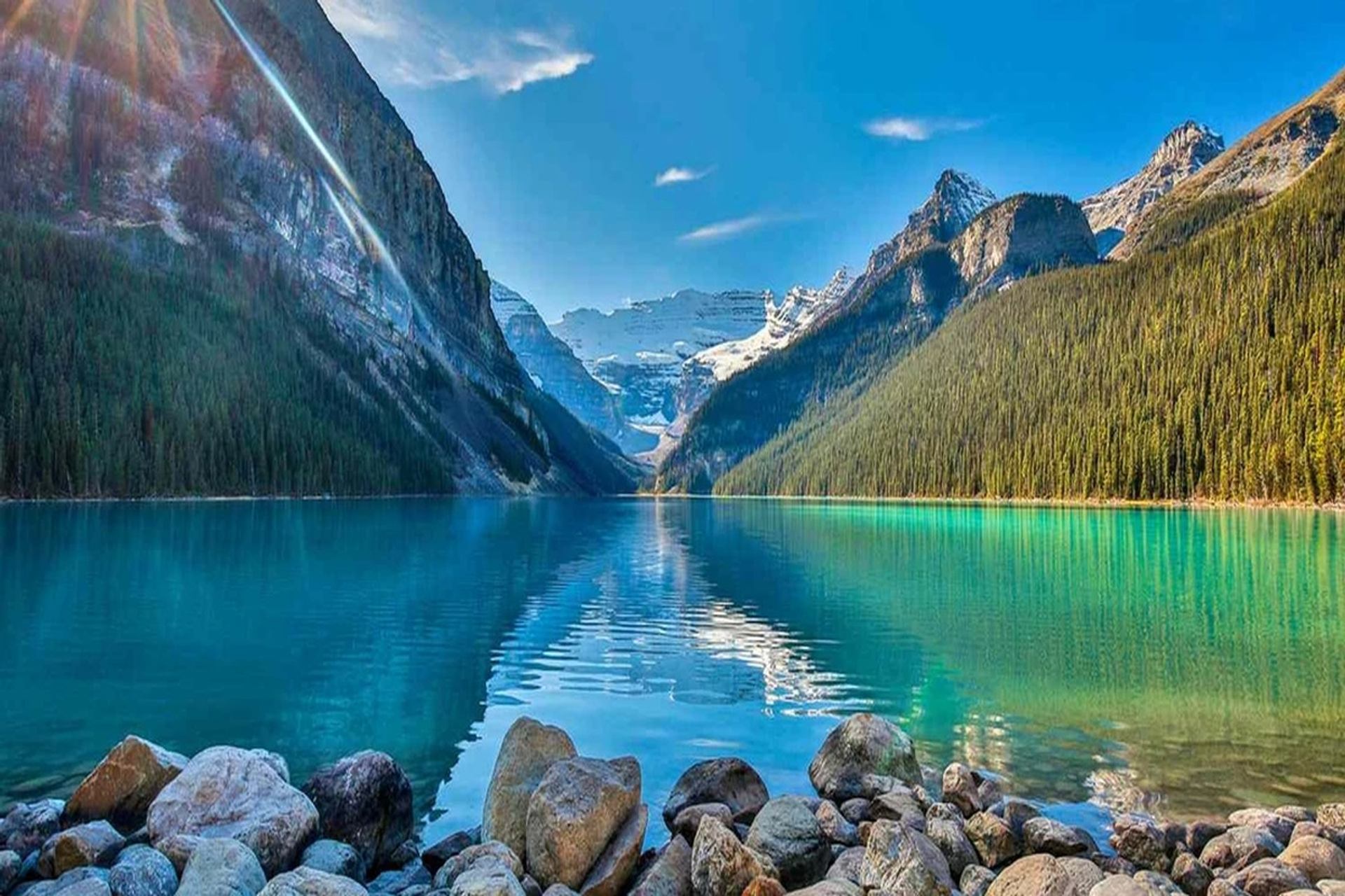 Turquoise mountain lake bordered by forested slopes, snowy peaks and a rocky shore.