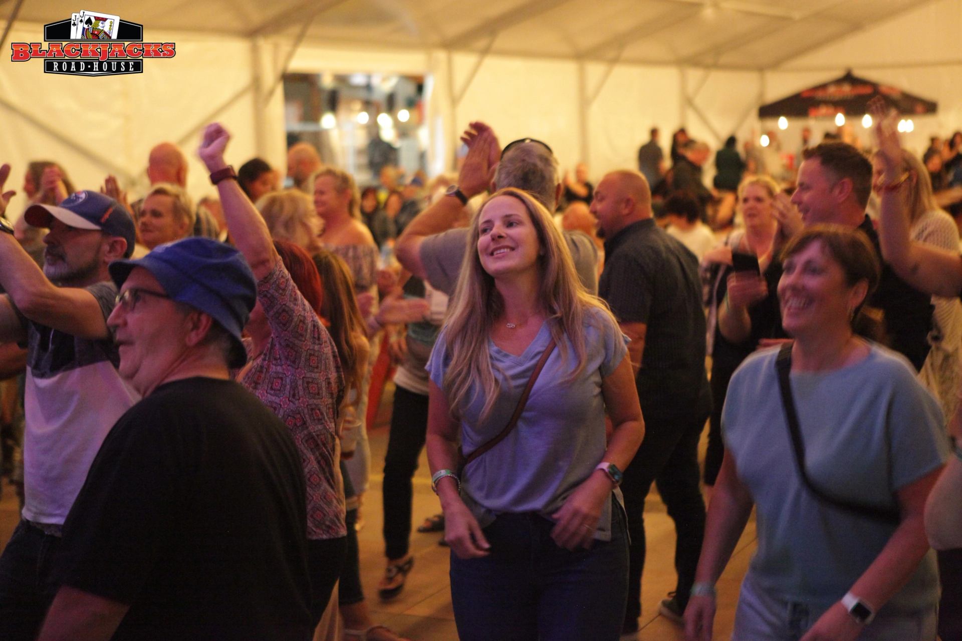Concert crowd dancing inside Blackjacks Road House tent with stage lights in background.