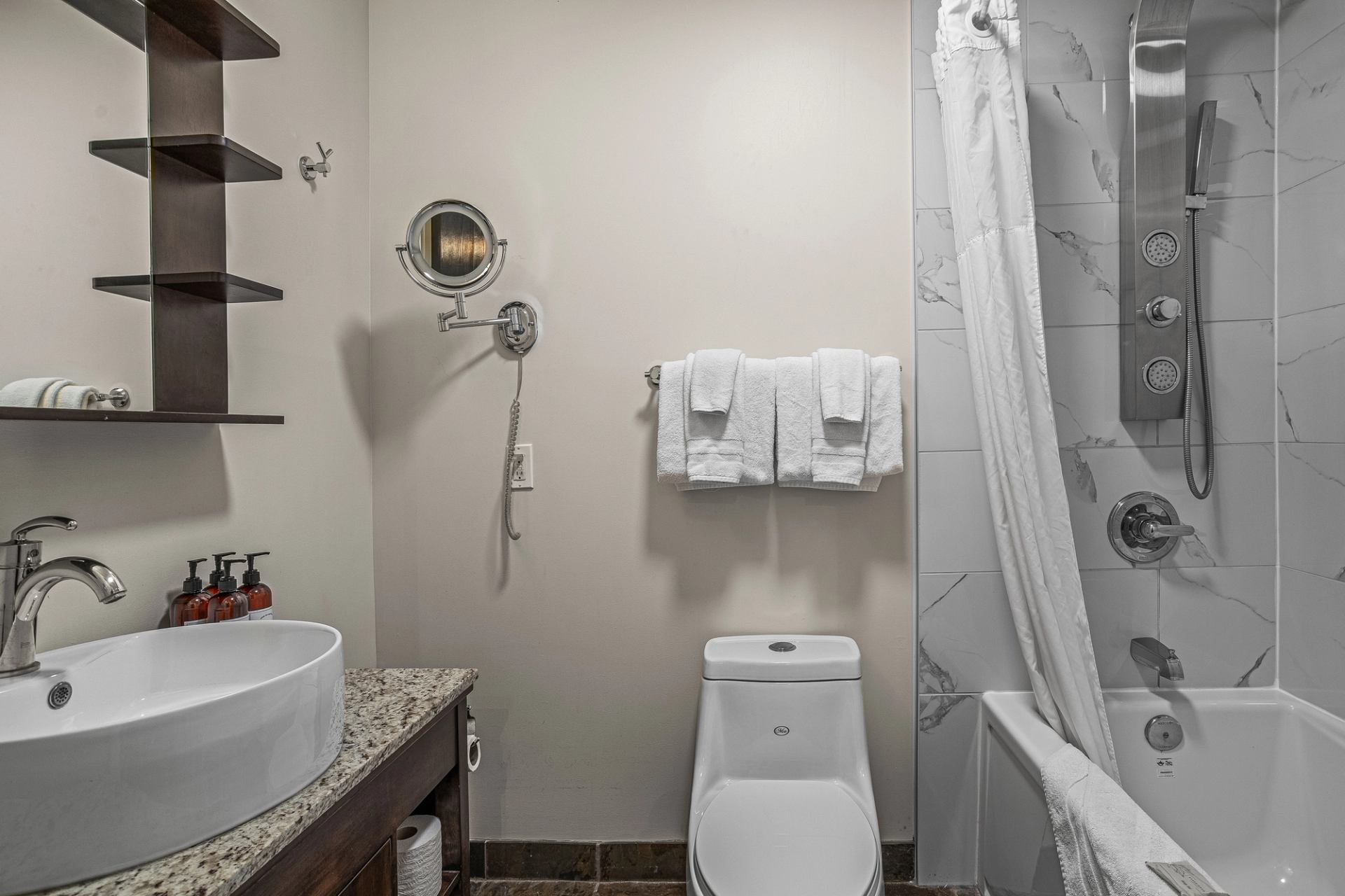 Bathroom with vessel sink, toilet, towel rack and marble-tiled bathtub shower.