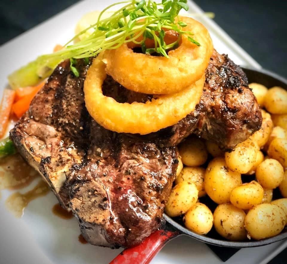 Grilled steak with onion rings, potatoes, and veggies on a white plate.