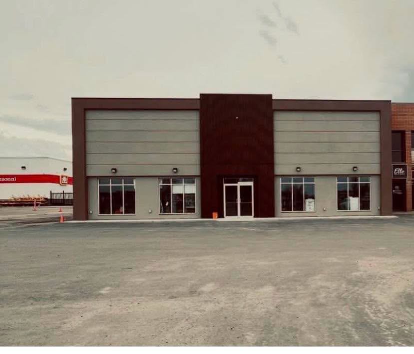 Commercial building with large windows and a vacant gravel lot.