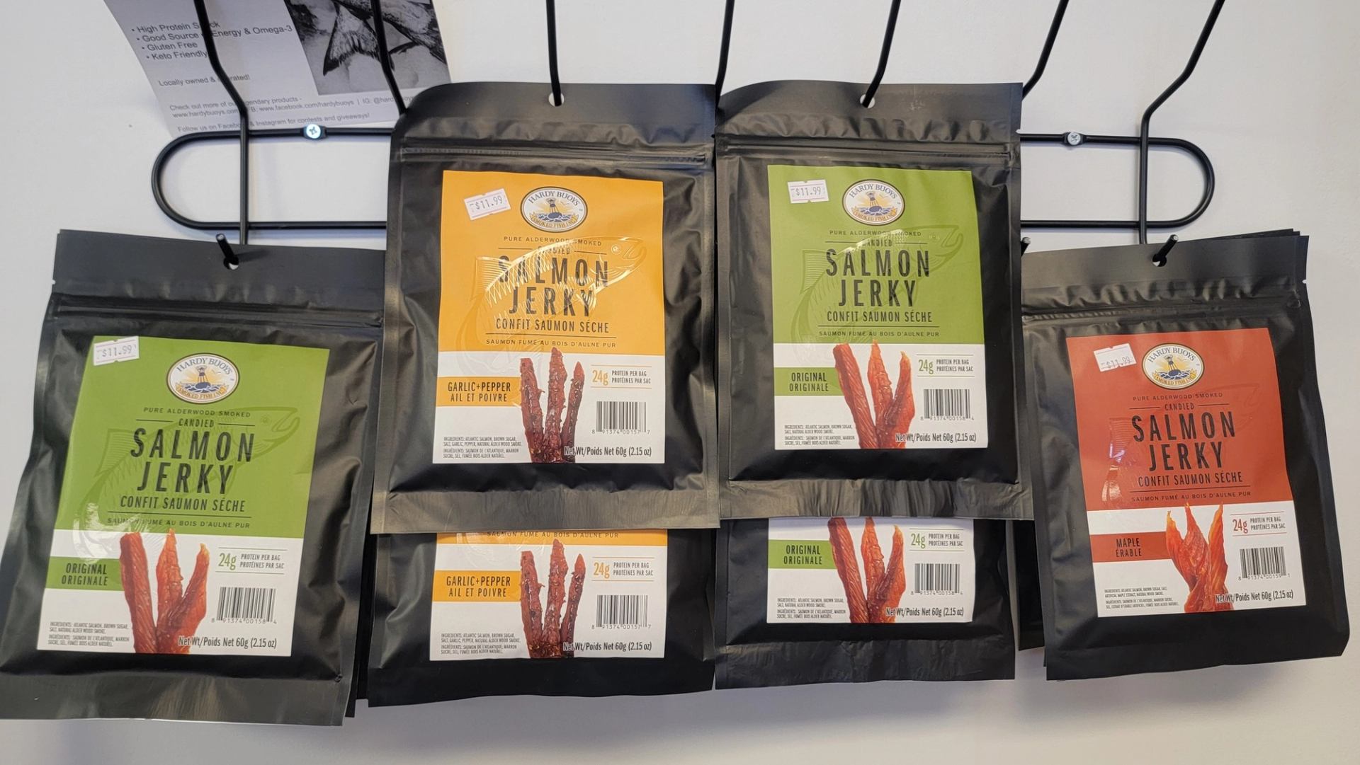 Six salmon jerky packs in green, orange, and red hang on a rack, each labeled with salmon strips.
