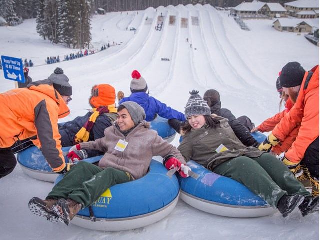 People in snow gear ride blue inflatable tubes on a snowy hill at Mt Norquay Tube Town.