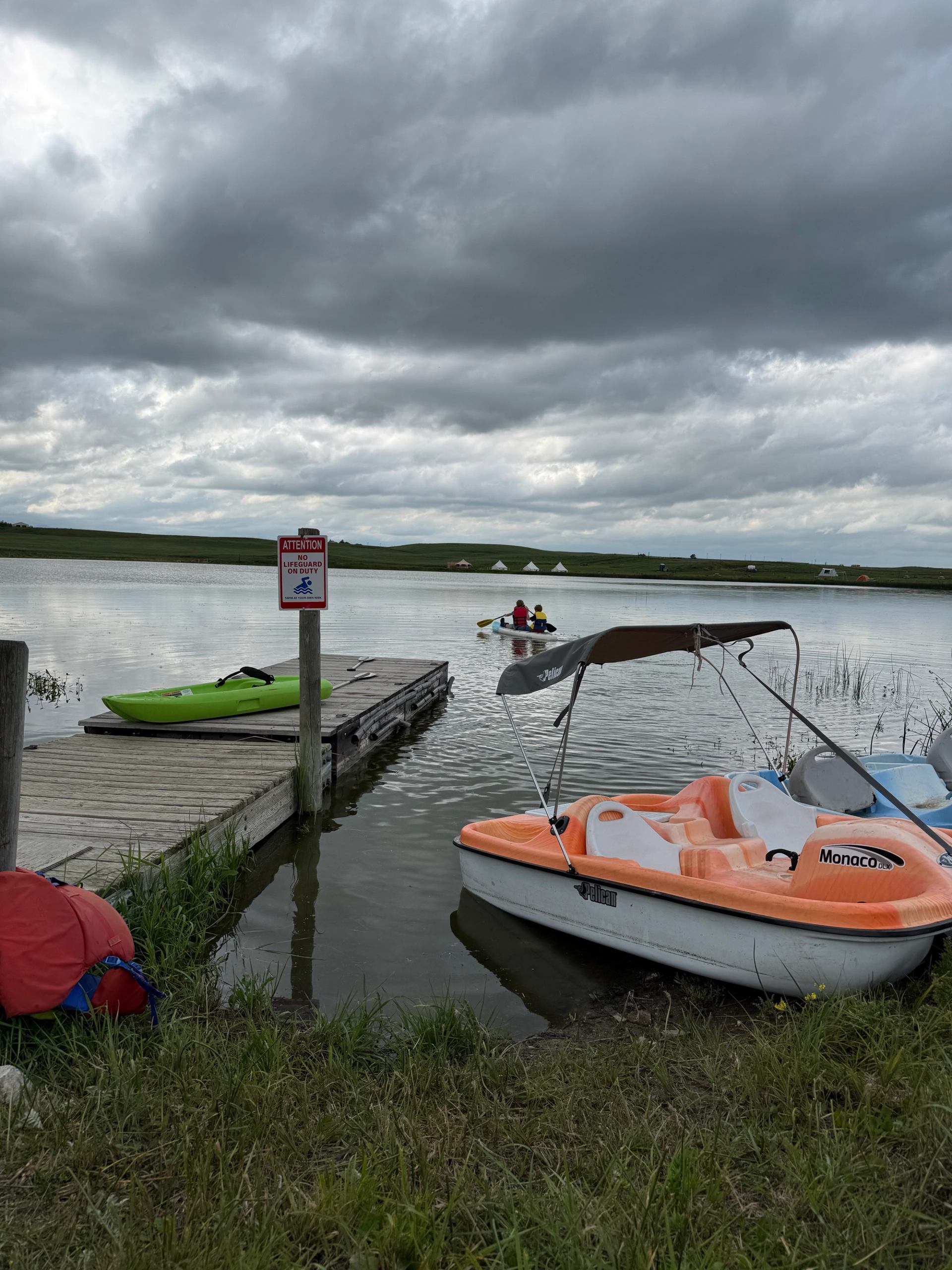 A dock with kayaks and paddle boats on a calm lake under cloudy skies.