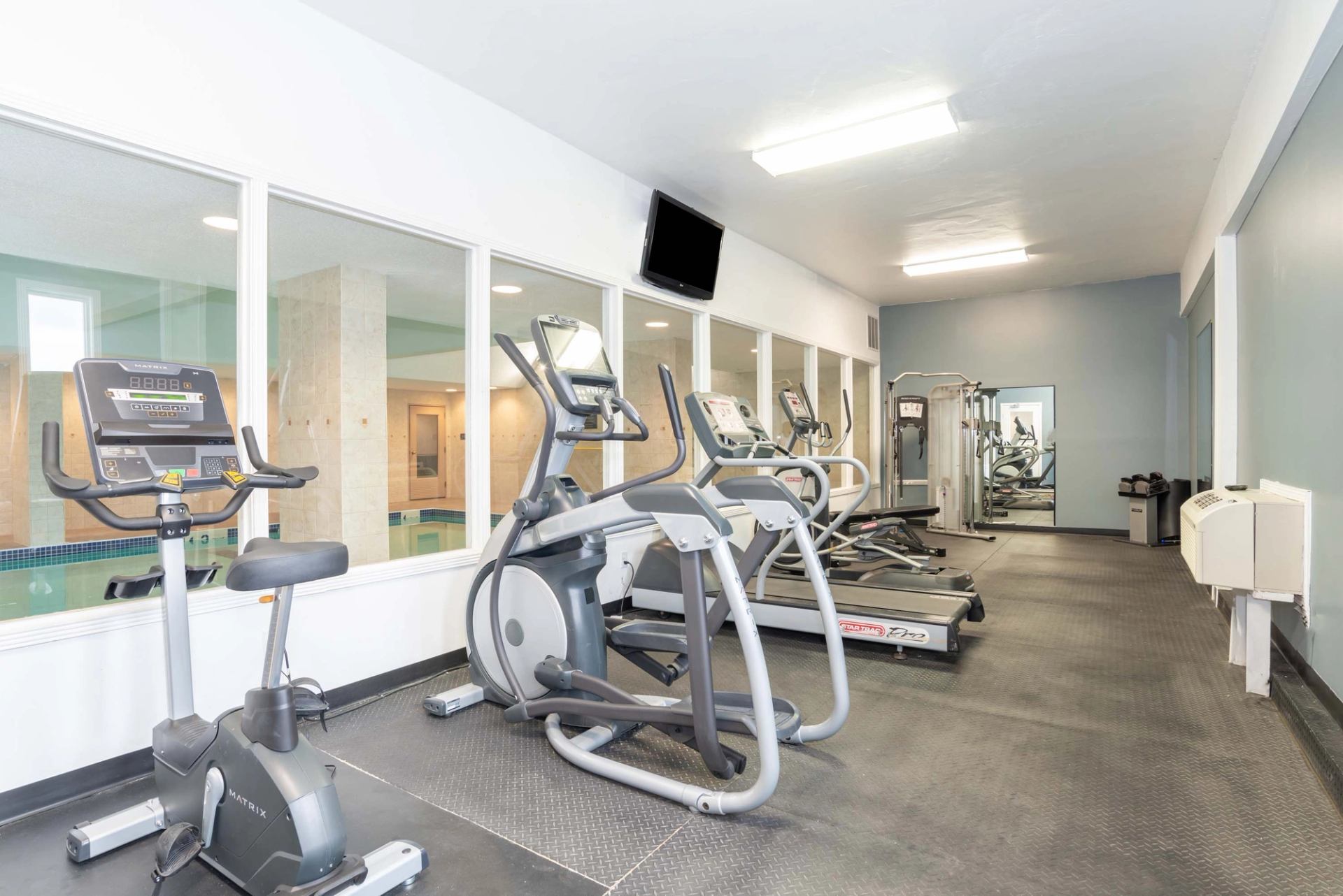 Hotel fitness room with cardio machines and windows overlooking the pool.