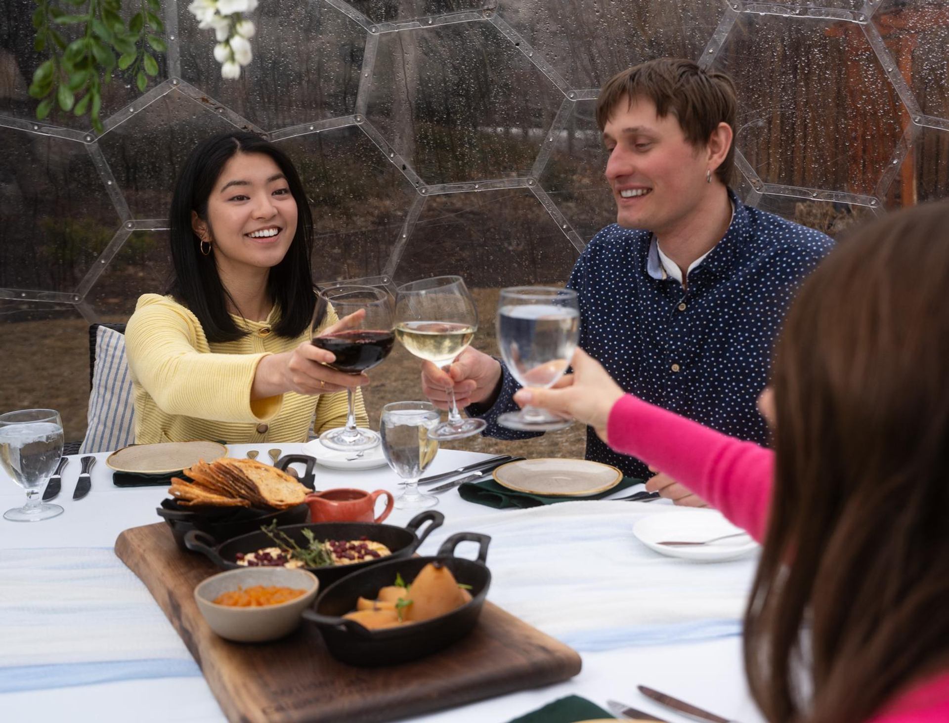 A small group clinks glasses together over a brunch table inside a garden dome.