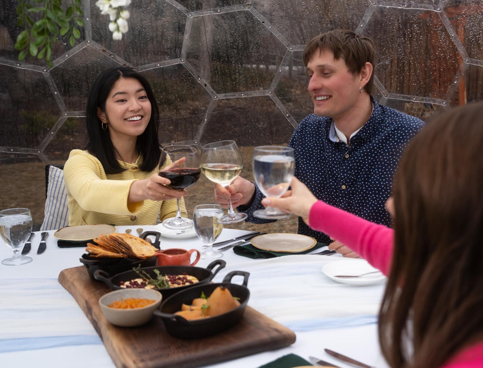 A small group clinks glasses together over a brunch table inside a garden dome.