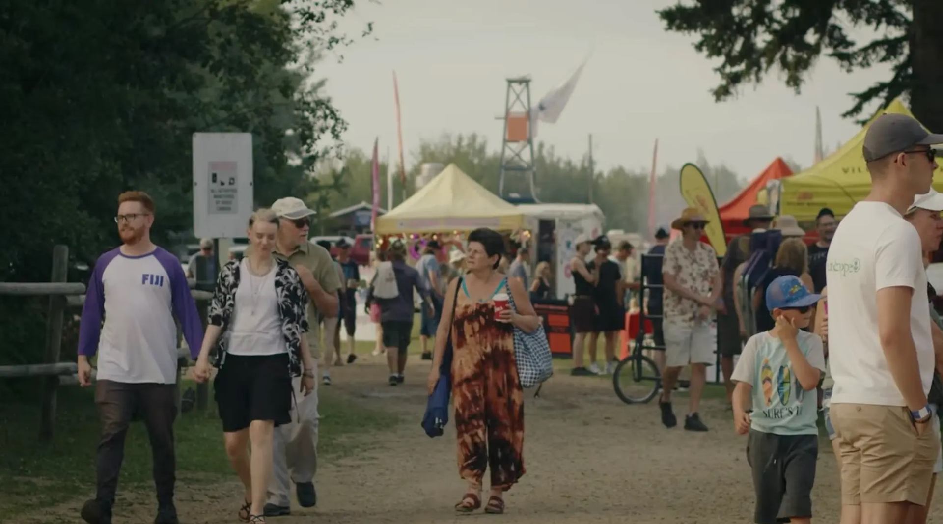 People walking through the festival grounds with tents, vendors, and trees in the background.
