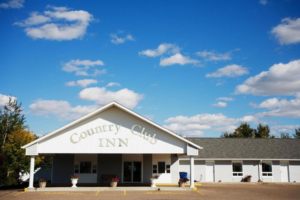 White Country Club Inn building with pitched roof and potted plants under blue sky.