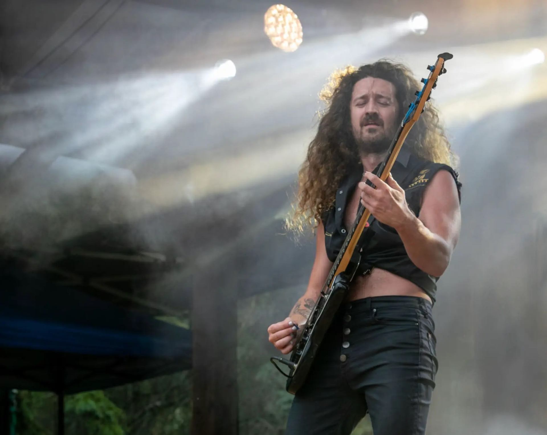 A guitarist performing on an outdoor stage with dramatic lighting and rising smoke effects.