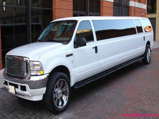 White stretch limo with chrome wheels parked on brick street in front of red-brick building.