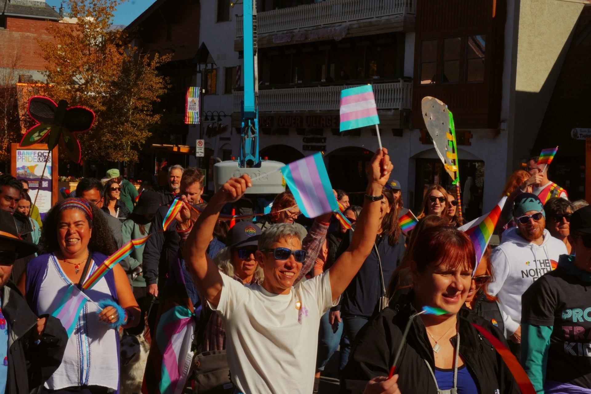 Pride march participants wave transgender and rainbow flags on a crowded street.