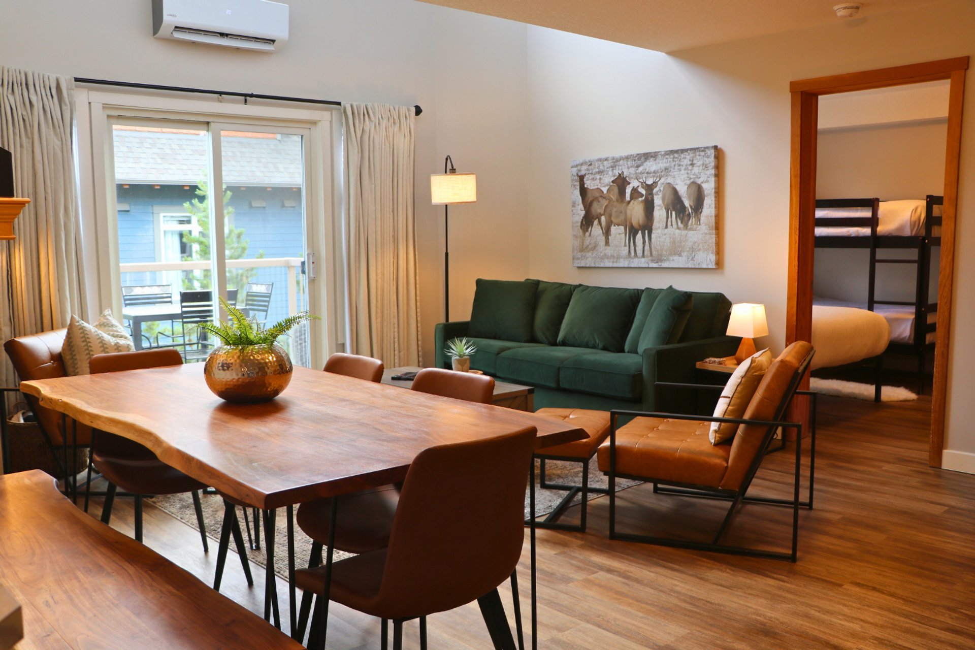 Open-plan dining and living room with wooden table, green sofa and adjoining bunk room.