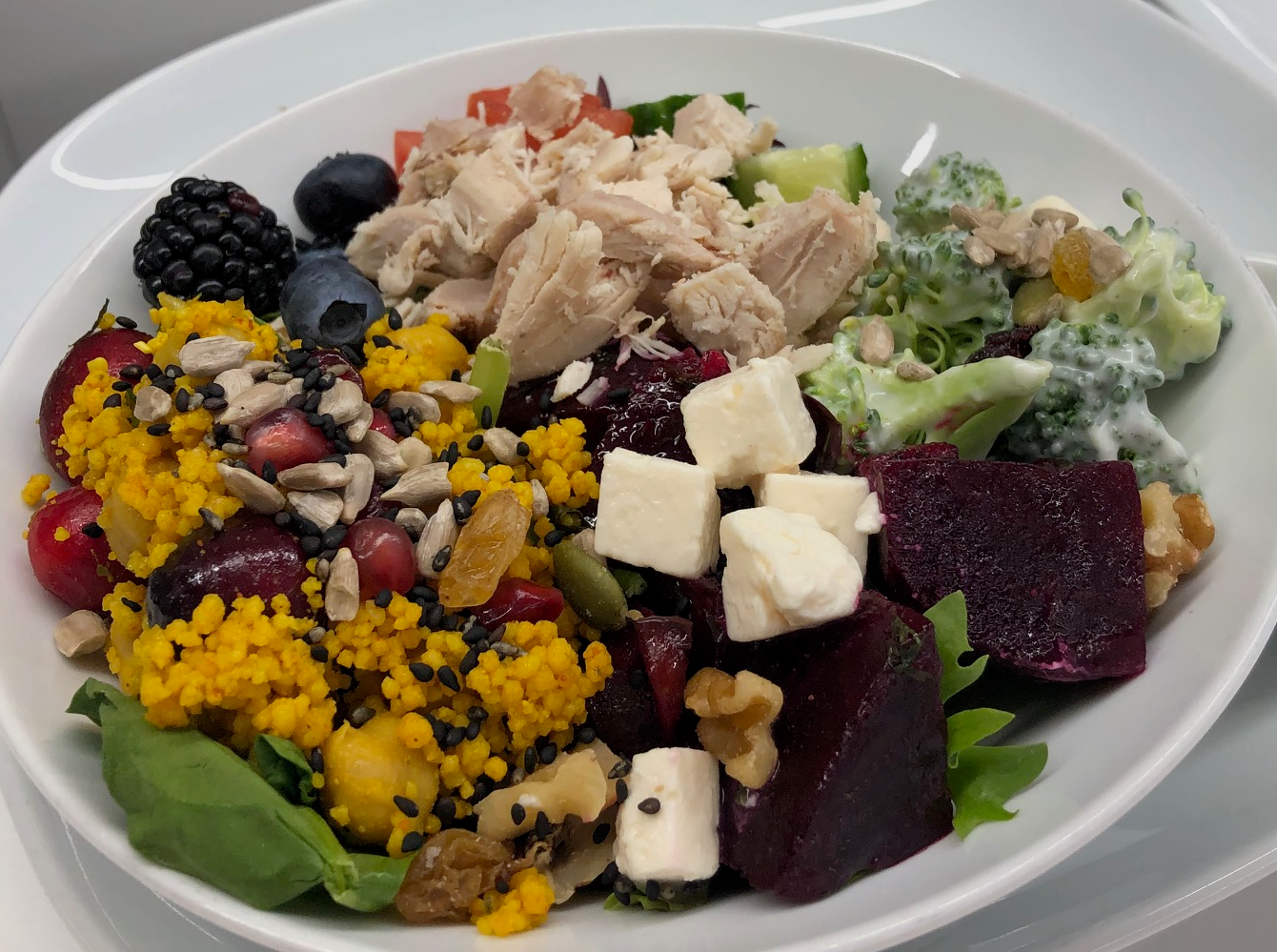 Colourful salad bowl with couscous, beets, feta, berries, seeds and shredded chicken.