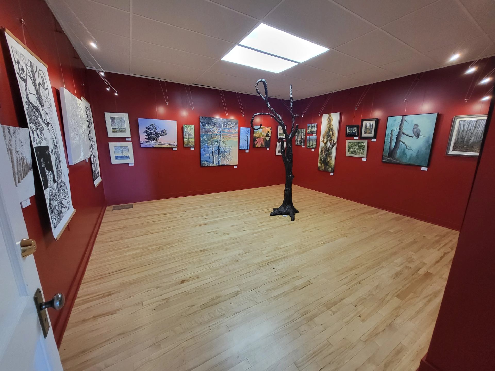 Open gallery space with red walls, wooden floors, and artwork hung throughout.