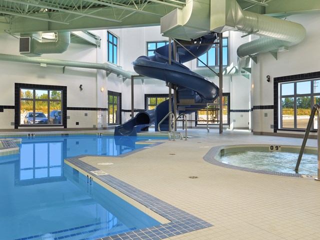 Indoor pool with blue waterslide, hot tub, and large windows.