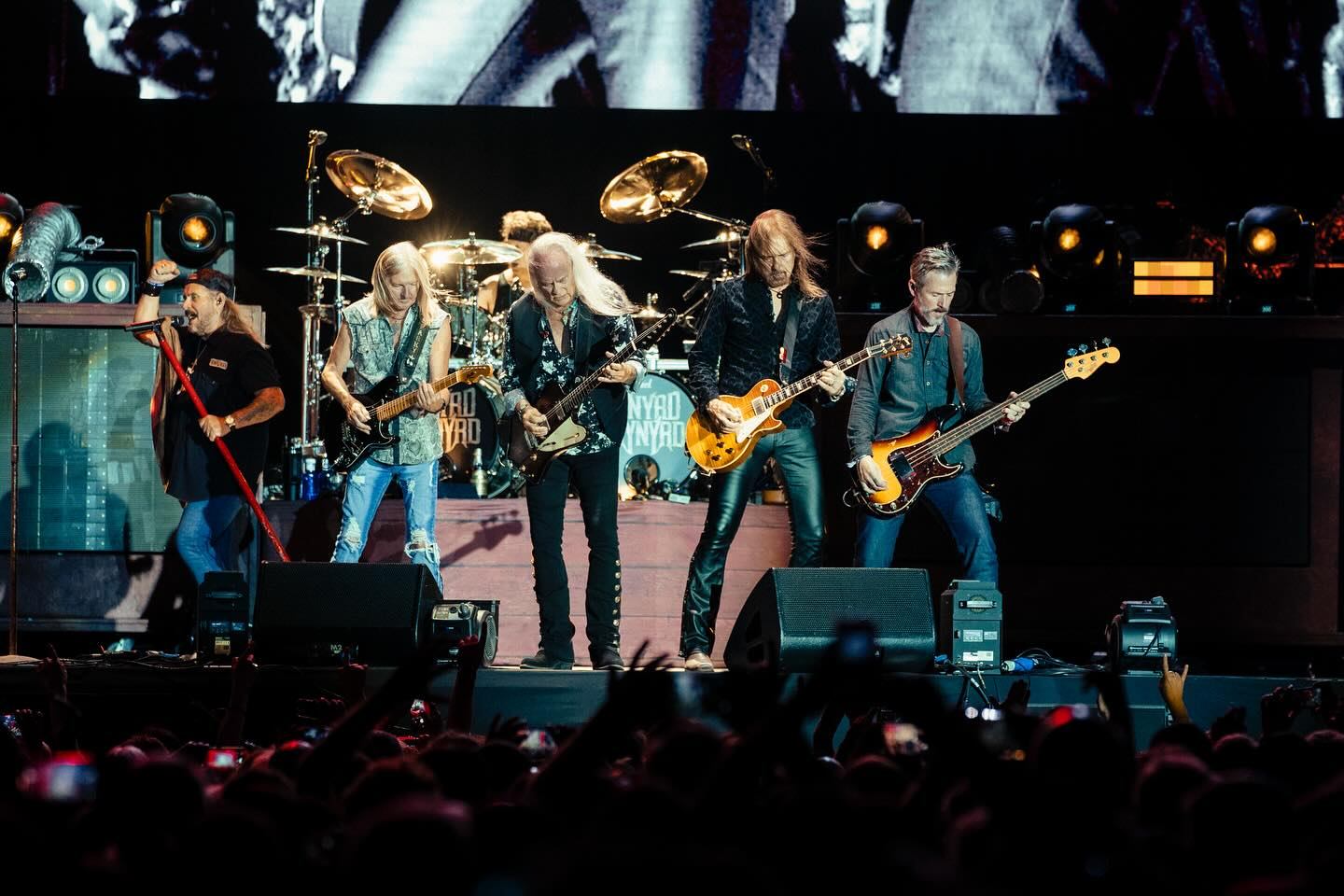 Lynyrd Skynyrd performs live on stage with guitars, drums, and bright lights before a large crowd.