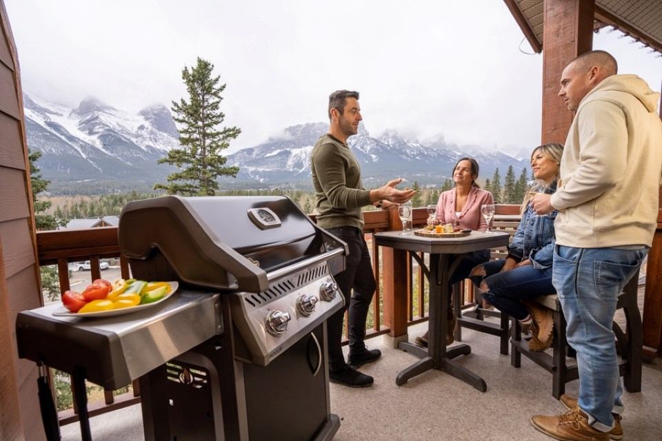 Mountain-view lodge balcony with barbecue grill and four people seated at a table.