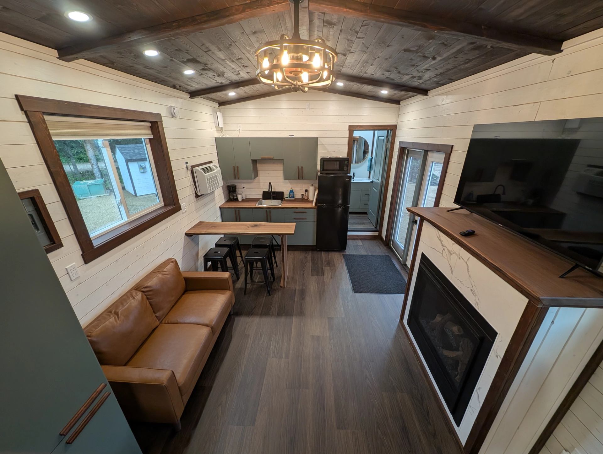 Tiny home interior with kitchen, leather sofa, fireplace and wall-mounted television.