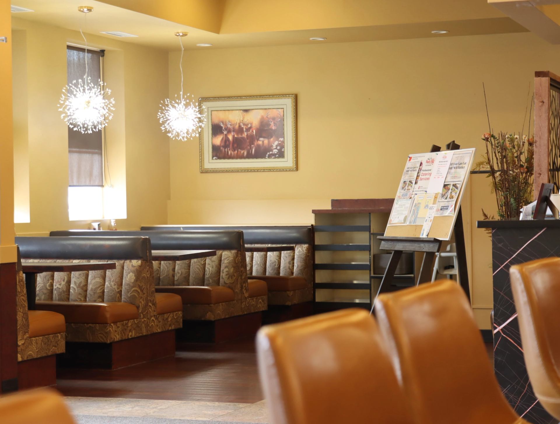 Restaurant interior with empty booths, modern pendant lights and brochure stand near entrance.