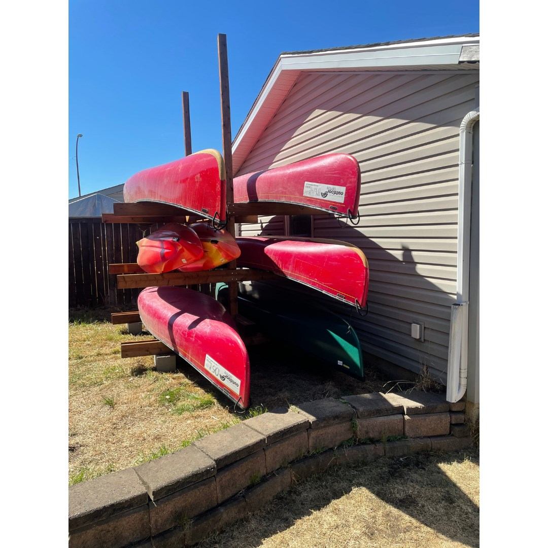 Four red kayaks stacked on a wooden rack beside a building under clear skies.