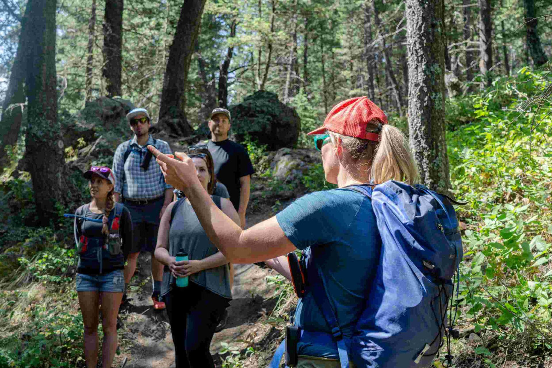 Guide speaking to hikers gathered on a wooded trail.